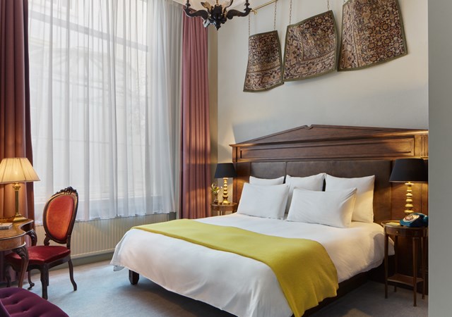 A well-appointed hotel room showcasing a bed, a chair for relaxation, and a lamp providing warm light.
