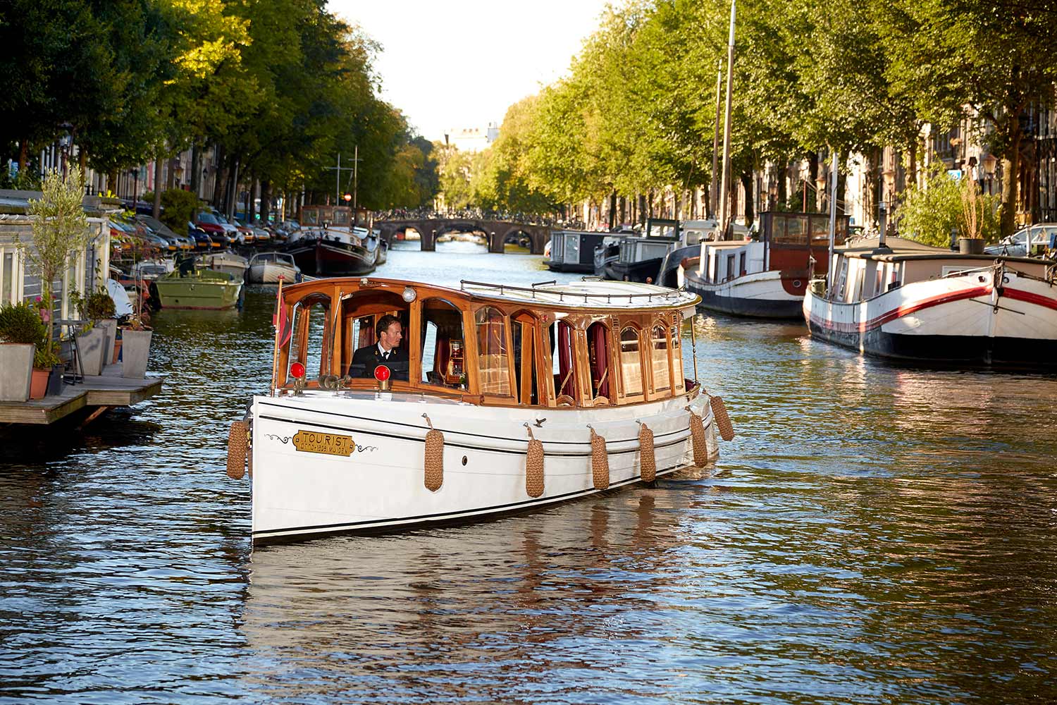 A boat glides through a city canal, surrounded by urban architecture and reflecting water on the Amsterdam canals.