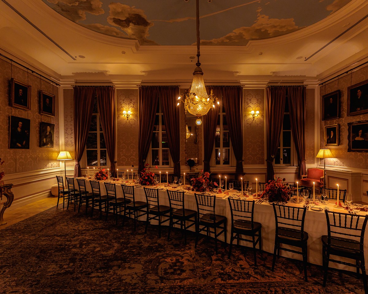 Long dining table set with candles and floral arrangements in an elegant room with chandeliers and classic artwork.