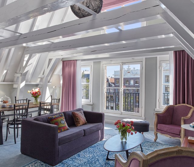 An inviting living room at Pulitzer Amsterdam with a striking purple couch and a contemporary table, perfect for relaxation and gatherings.