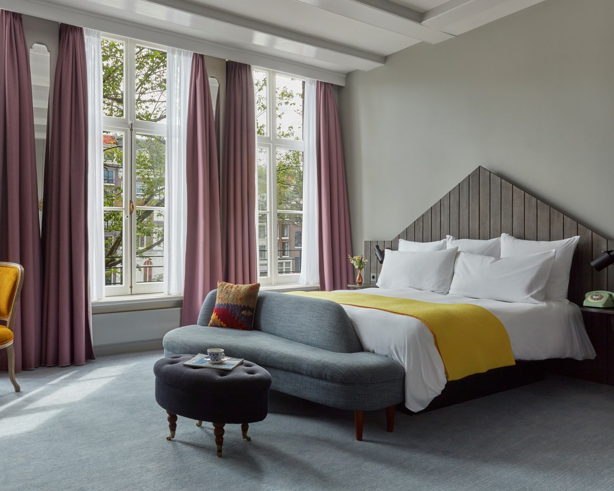 A cozy hotel room featuring a neatly made bed, a comfortable chair, and a window allowing natural light to enter.