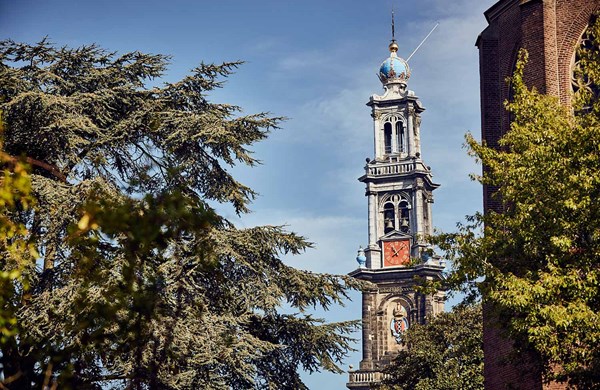 Close-up of the Westerkerk tower in Amsterdam, showcasing its blue dome, golden crown, and red clock face with a clear sky.