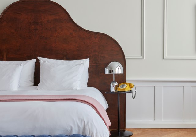 A minimalist bedroom featuring a wooden headboard, white bedding, and a yellow throw, accented by framed maps on the wall.