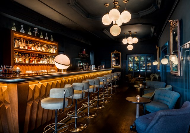 Stylish bar with dim lighting, leather bar stools, and a warm ambiance at Pulitzer Amsterdam.