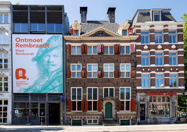 The Rembrandt House Museum, a historic brick building with red shutters, flanked by modern structures in Amsterdam.