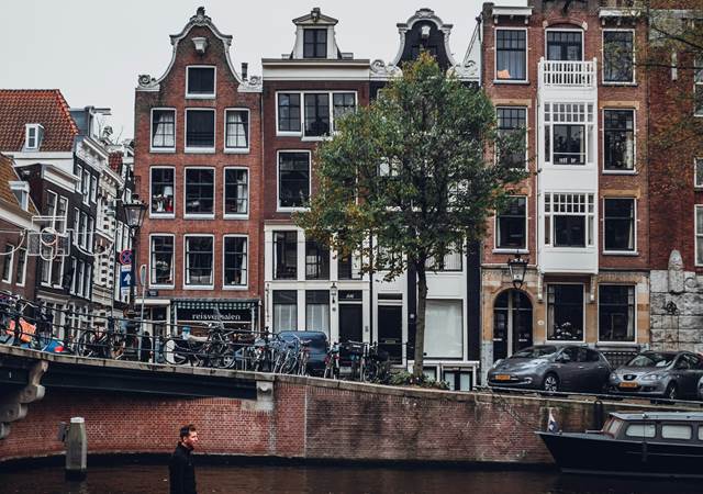 A man in a boat glides through a canal in Amsterdam, with urban buildings standing tall along the banks.