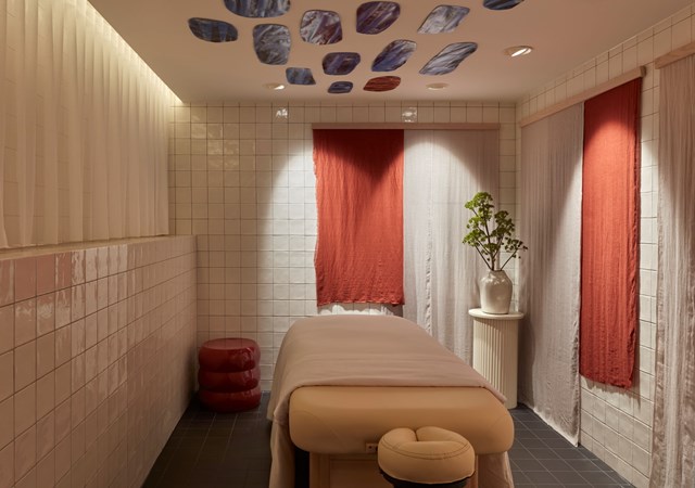 Cozy treatment room with a massage table, dim lighting, tiled walls, and red and beige drapes at Pulitzer Amsterdam.
