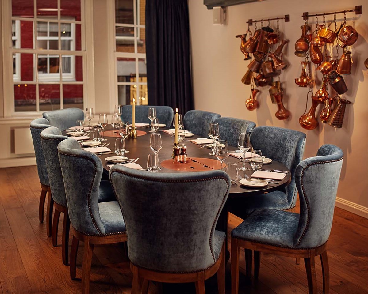 Cozy dining room with round table, blue velvet chairs, and vintage copper pots hanging on the wall at Pulitzer Amsterdam.