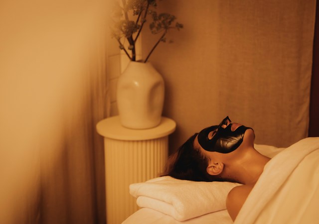 A woman wearing a black face mask, relaxing on a massage table in a peaceful and relaxing space.
