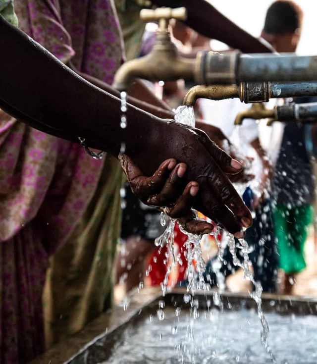 Close-up of hands under a flowing water faucet, symbolizing access to clean water.