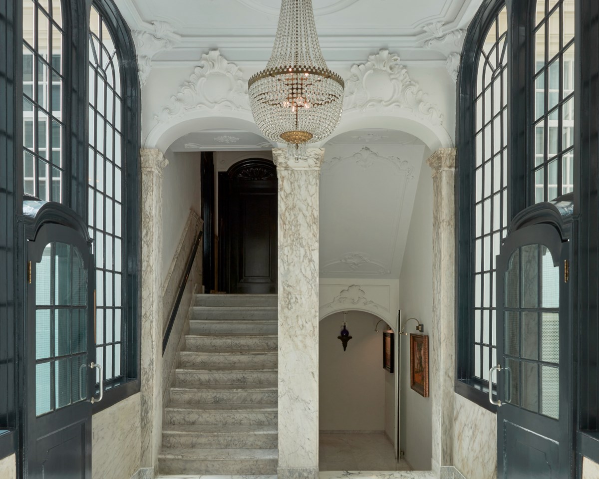 An opulent hallway adorned with a chandelier, leading to a beautifully crafted staircase, exemplifying luxury and style.