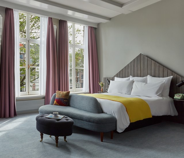 An inviting hotel room with a neatly made bed, a stylish chair, and a window that brightens the atmosphere.