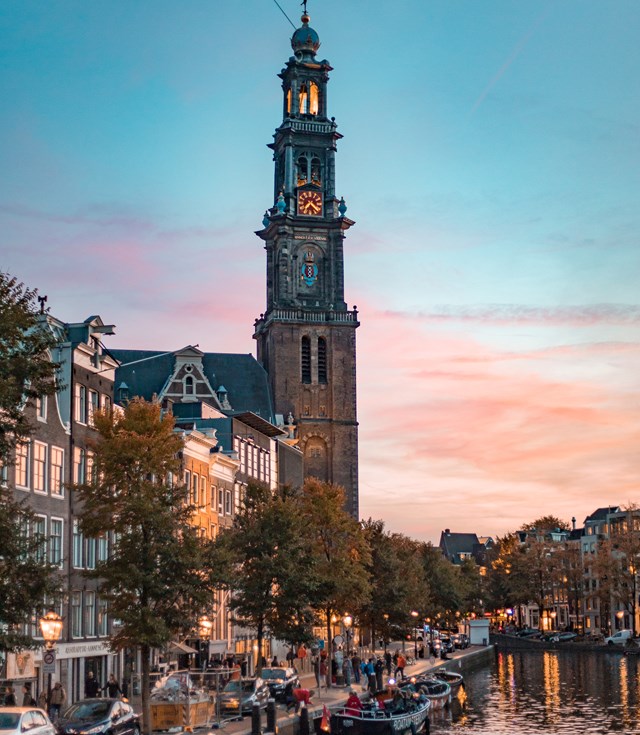 The Westerkerk tower in Amsterdam during sunset, with a soft pink and blue sky.