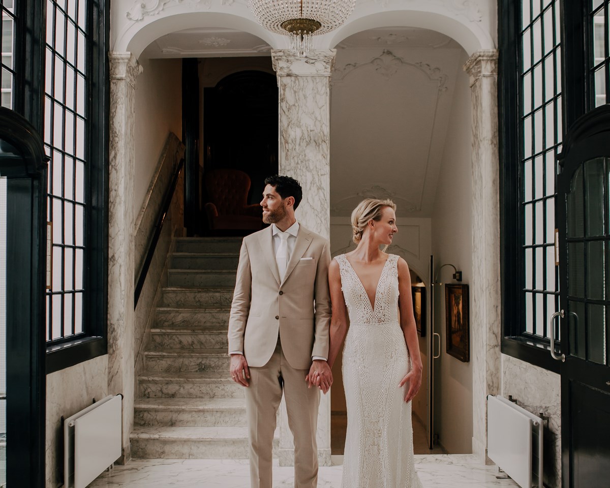 A bride and groom pose together in an elegant hallway, showcasing their love and the beauty of their wedding day.