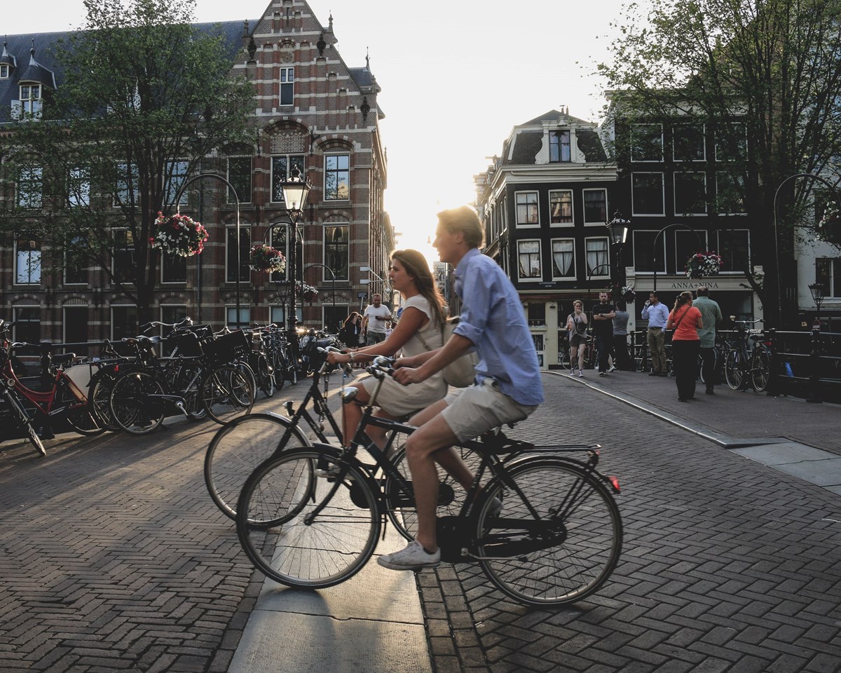 Two cyclists enjoying a scenic ride through Amsterdam, with historic buildings and serene waterways in the background.