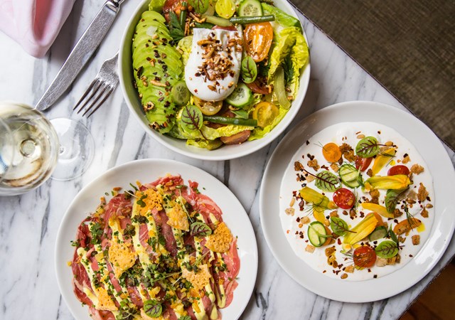 Three elegantly arranged plates of food displayed on a polished marble table, showcasing a variety of culinary delights.