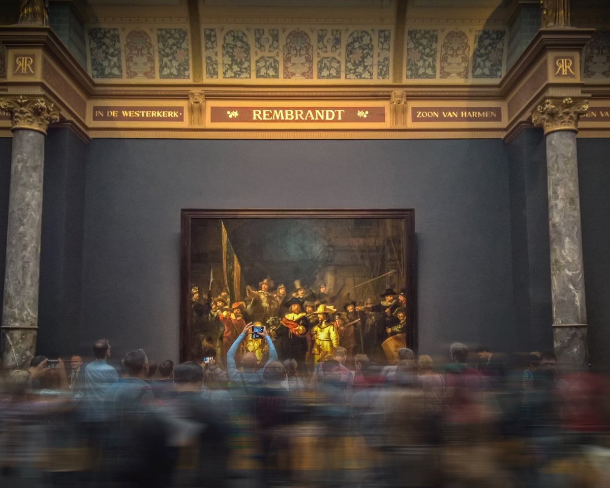 A gathering of individuals engaged in viewing a painting displayed in an exhibition space.