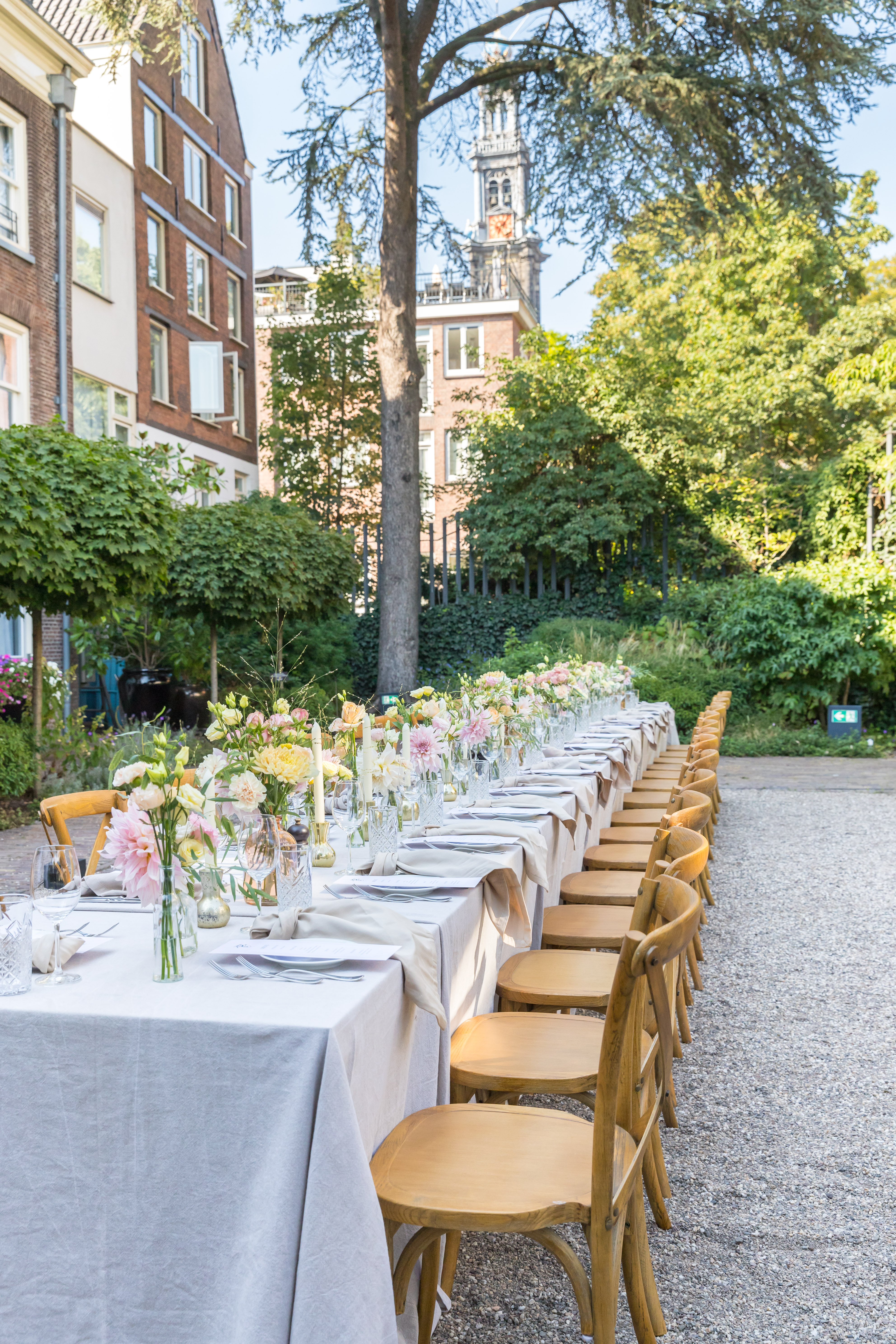 Long outdoor dining table set with flowers, candles, and glassware, with a church steeple in the background.