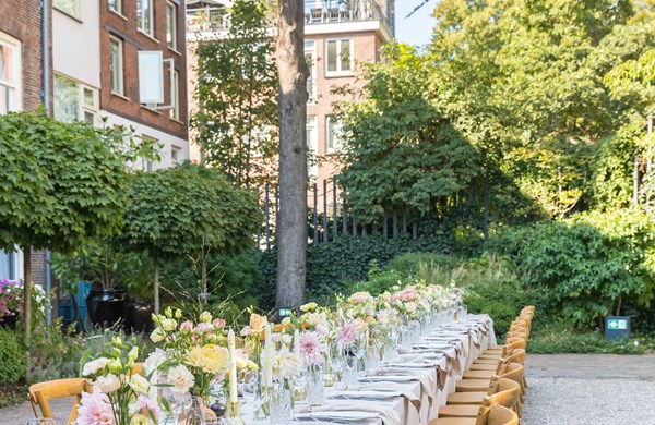 Long outdoor dining table set with flowers, candles, and glassware, with a church steeple in the background.