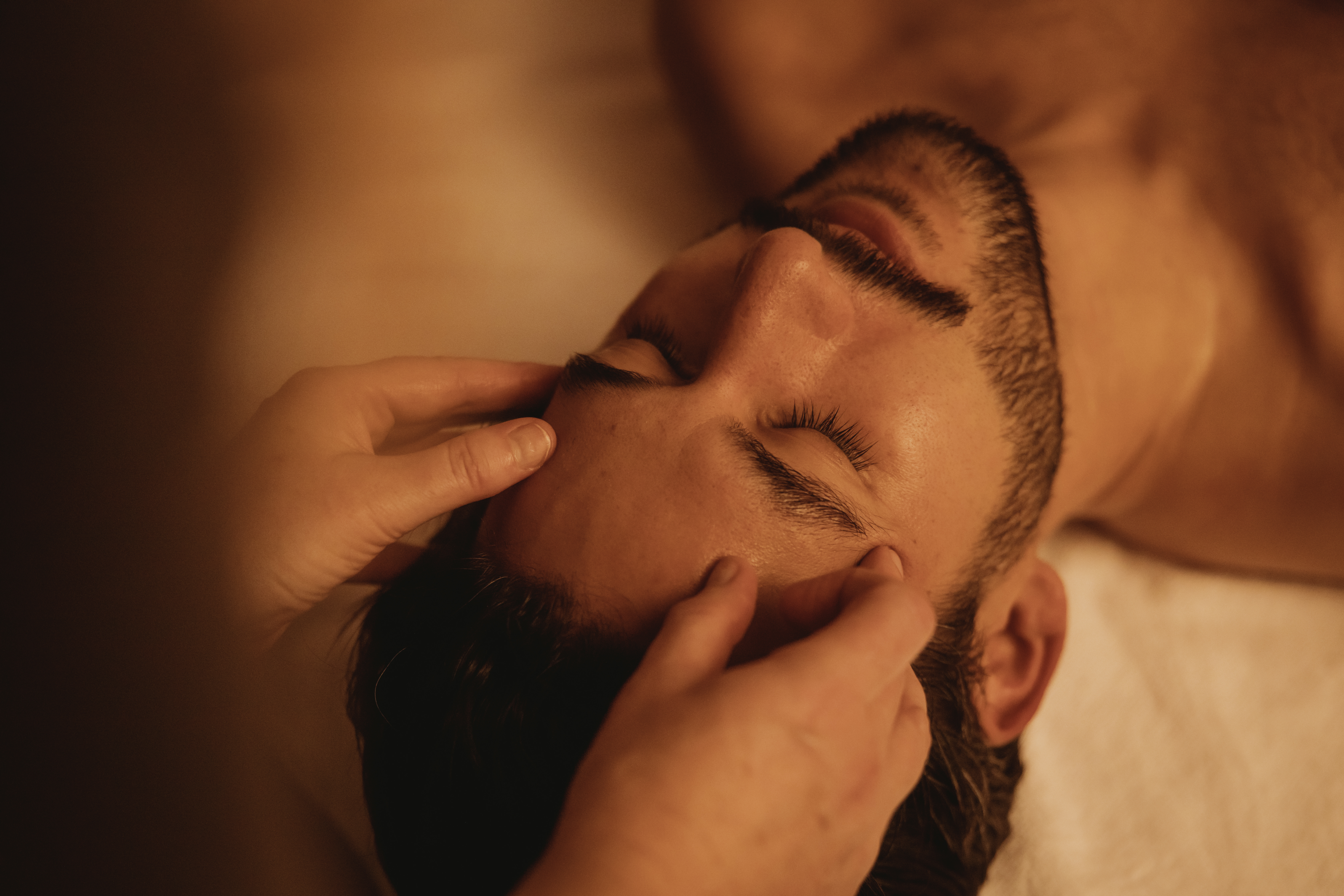 A man receiving a relaxing head massage, eyes closed, surrounded by warm lighting at the Pulitzer Amsterdam spa.
