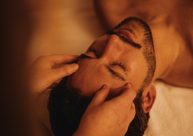 A man receiving a relaxing head massage, eyes closed, surrounded by warm lighting at the Pulitzer Amsterdam spa.