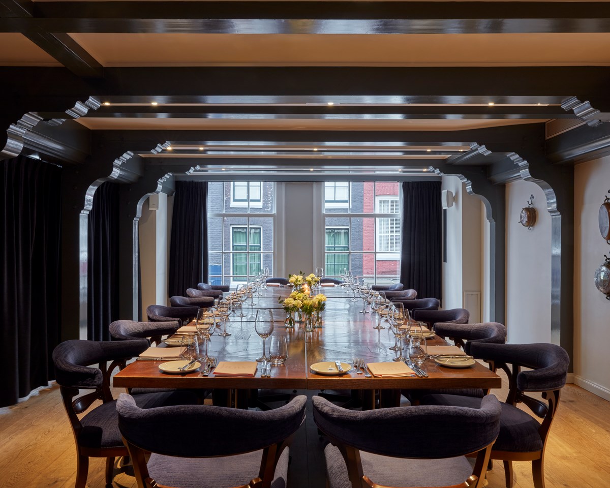 Elegant dining room at Pulitzer Amsterdam with a long table set with flowers, crystal glasses, and yellow napkins.