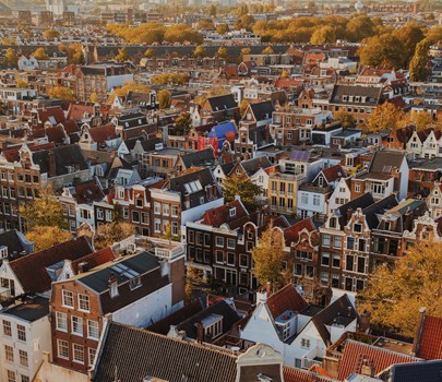 Rooftop view of Amsterdam's historic houses with steep gables and autumn foliage in warm sunlight.