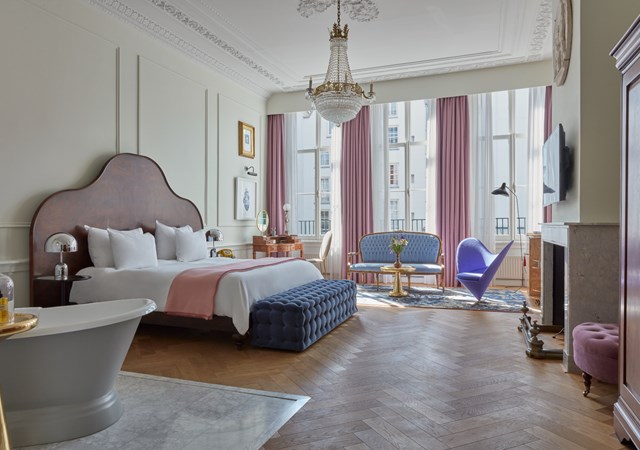 A spacious bedroom featuring a large bed, a bathtub, and a large window allowing natural light to fill the room.