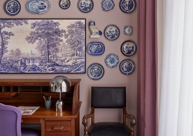 Desk area adorned with a collection of blue and white plates, a purple chair, and a vintage-style lamp.