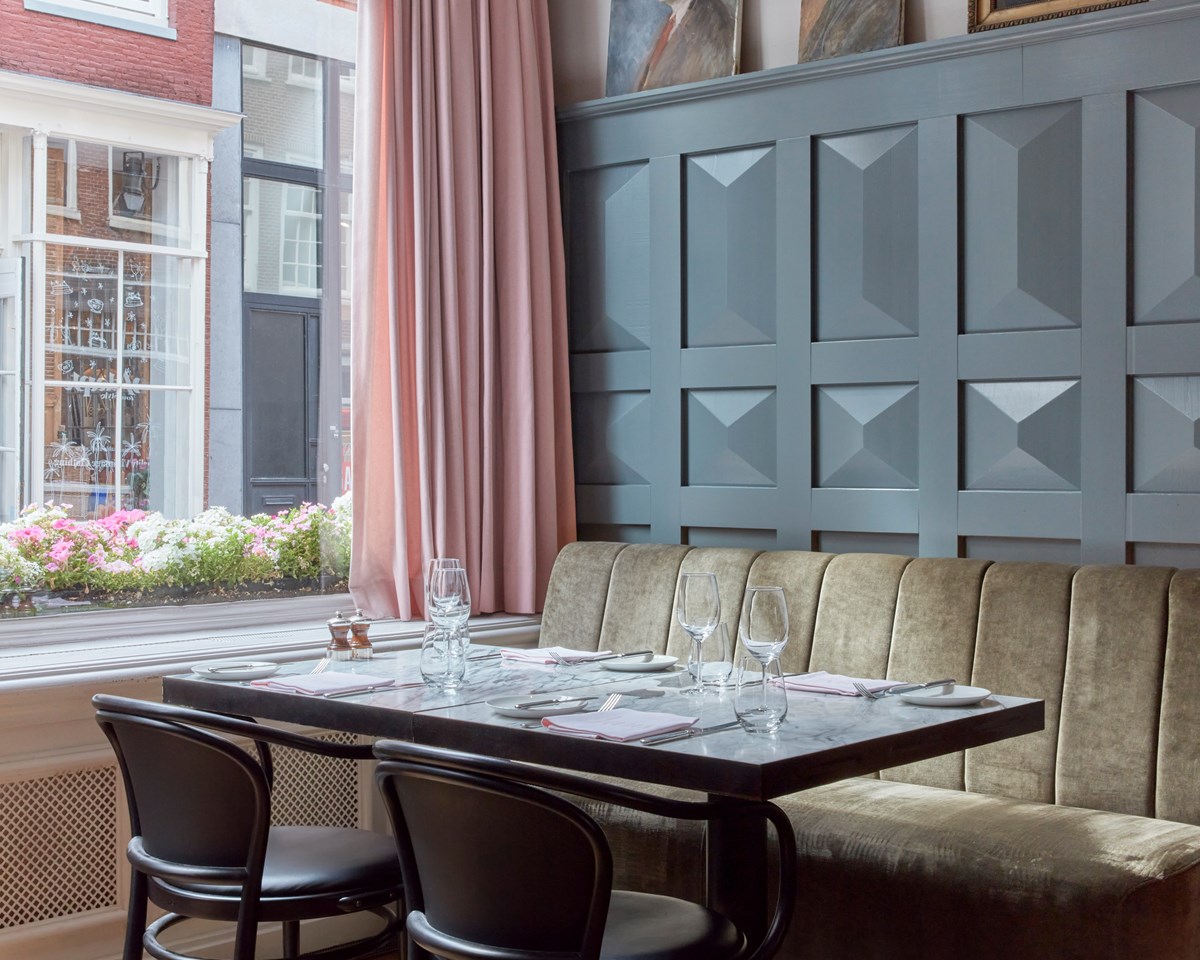Intimate restaurant booth at Jansz. in Amsterdam with plush seating and a table set for four, against a textured gray wall.