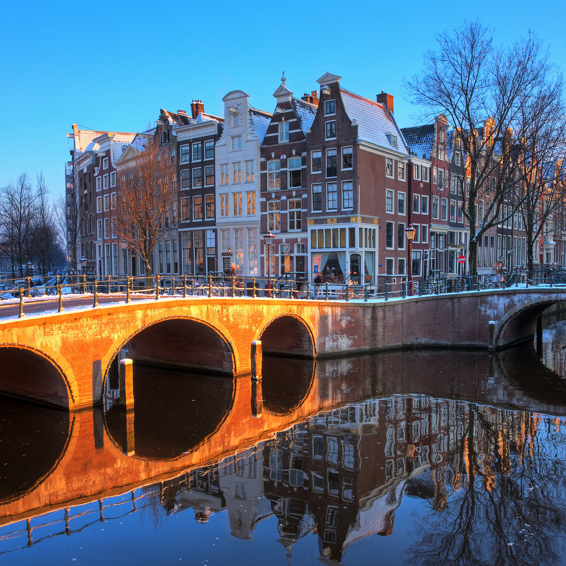 A picturesque winter scene in Amsterdam, showcasing snow-covered canals and charming architecture under a clear sky.