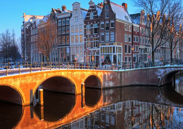 A picturesque winter scene in Amsterdam, showcasing snow-covered canals and charming architecture under a clear sky.