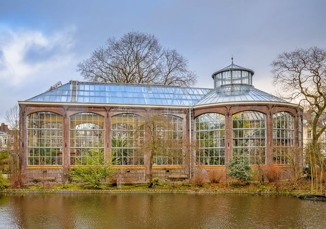A large building featuring a glass roof surrounded by lush green trees, showcasing a harmonious blend of nature.