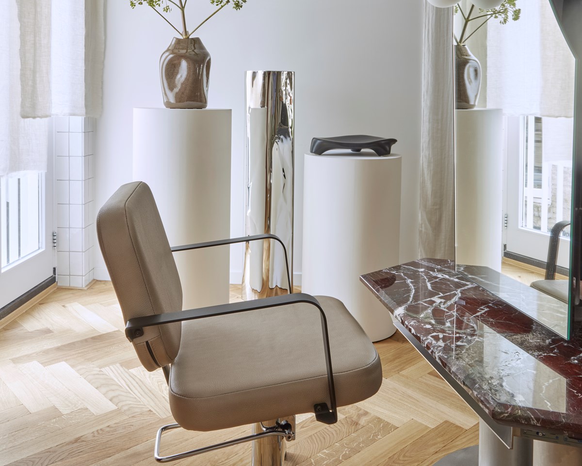 Minimalist interior with a sleek salon chair, marble table, and decorative vases on pedestals in a bright space.