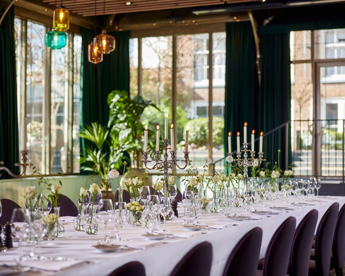 A long dining table elegantly arranged for a dinner party in a spacious, well-decorated room.