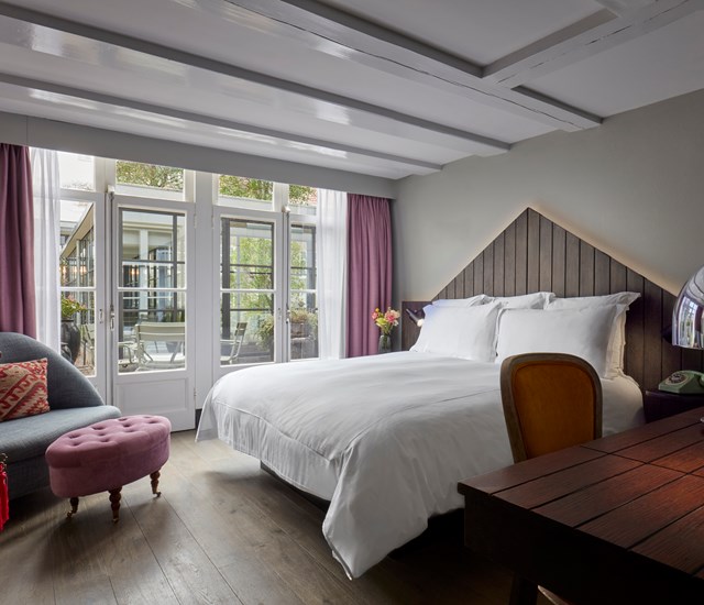 Pulitzer Amsterdam hotel room with a cozy bed, purple curtains, and access to a private terrace through glass doors.