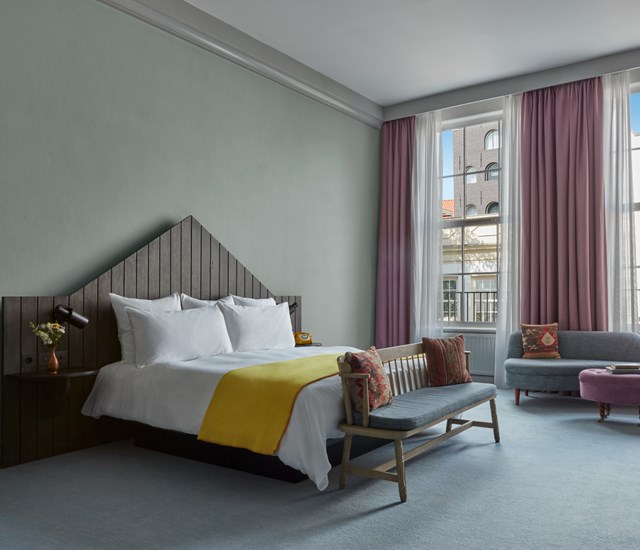 An inviting hotel room with a neatly made bed, a stylish chair, and a window providing ample daylight.