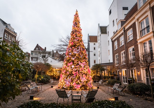 In the heart of a quaint courtyard, a vibrant Christmas tree is adorned with ornaments, creating a festive atmosphere.
