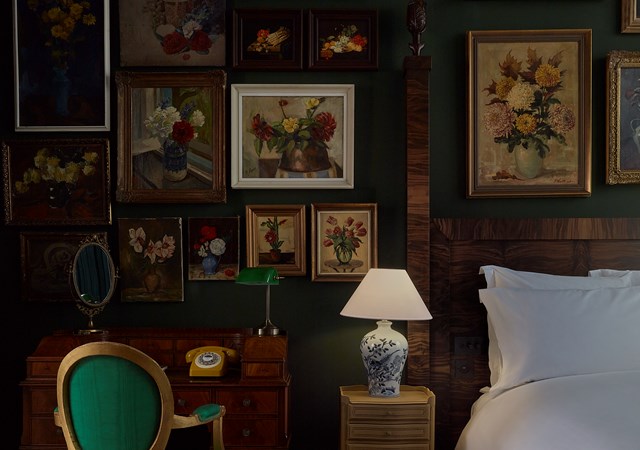 A serene bedroom with a neatly made bed, a functional desk, and artistic pictures displayed on the walls for decoration.