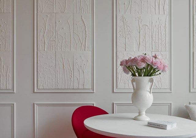A white table accompanied by red chairs positioned against a wall panel, creating a vibrant dining area.