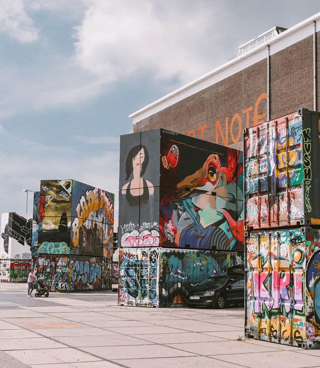 A vibrant street scene featuring colorful boxes and striking graffiti art on the walls, showcasing urban creativity.