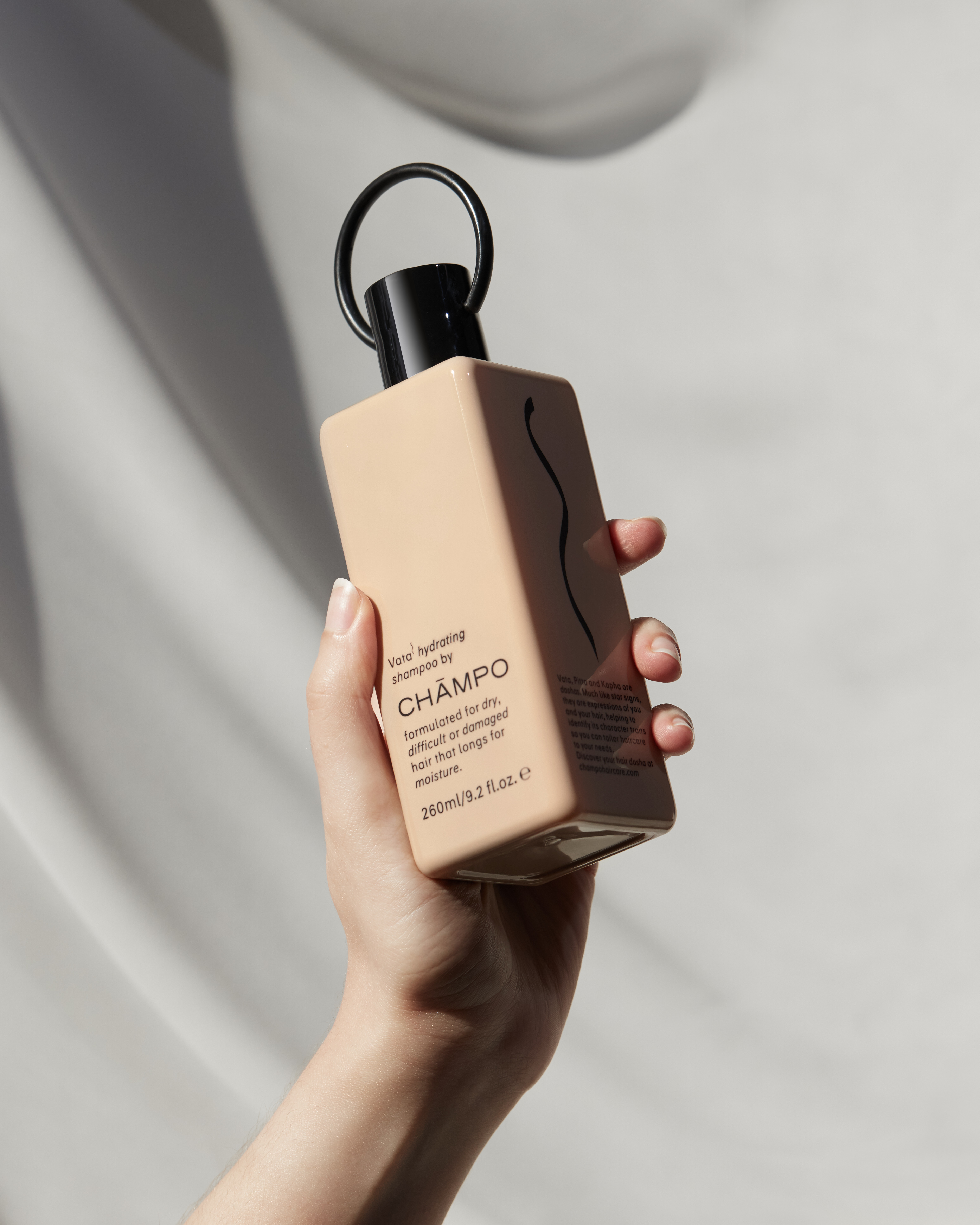 A woman gracefully holds a bottle of shampoo, showcasing its elegant design and luxurious appeal.