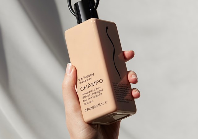 A woman gracefully holds a bottle of shampoo, showcasing its elegant design and luxurious appeal.