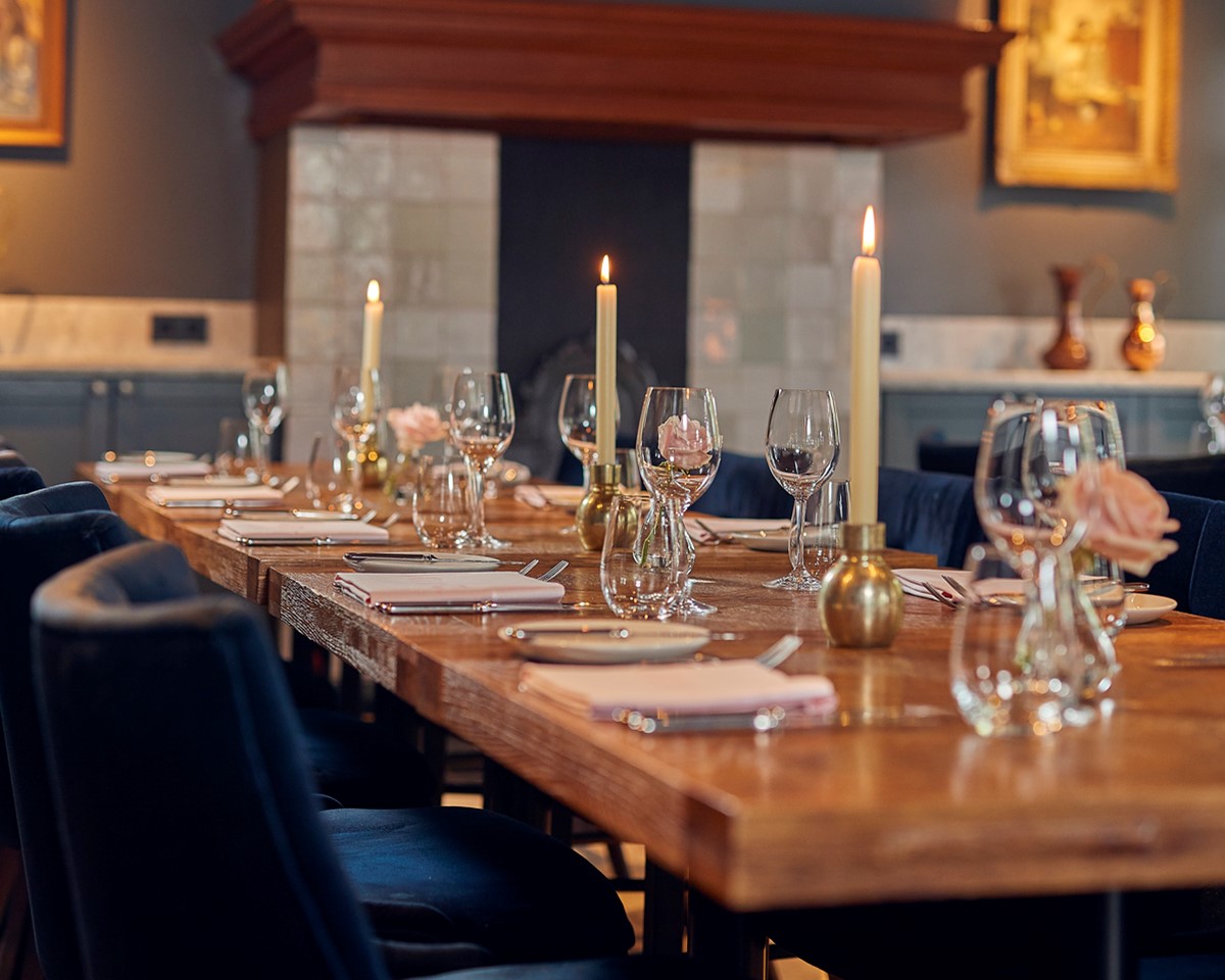 A long dining table elegantly set with candles and place settings, creating a warm and inviting atmosphere for guests.