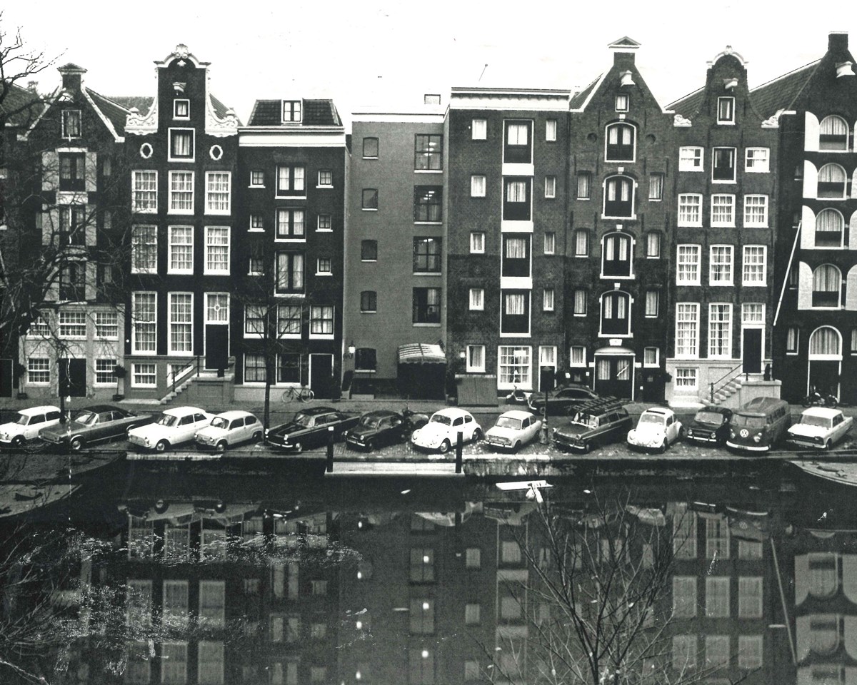A monochrome photo depicting a canal with parked cars alongside, illustrating a calm urban environment.