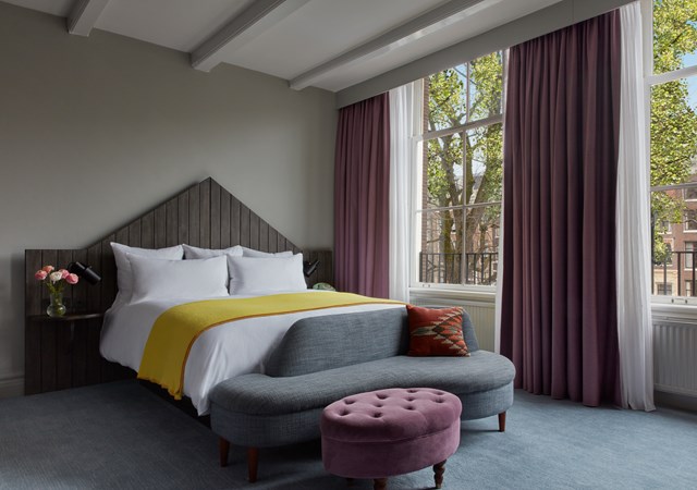 A neatly made bed featuring a yellow and gray blanket, complemented by a vibrant purple ottoman nearby.