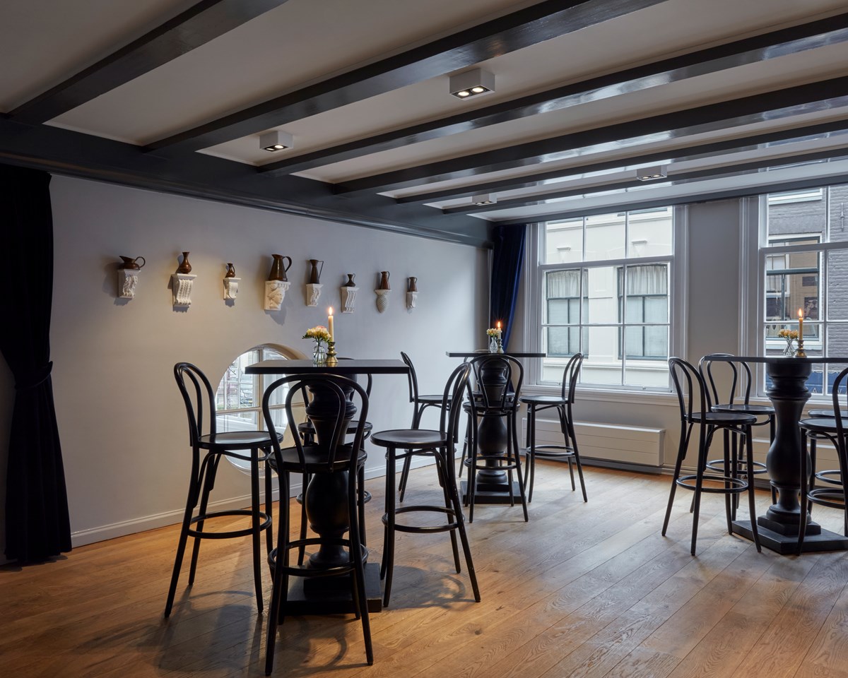 Modern lounge with tall black chairs, wooden floors, and decorative pottery on wall mounts.